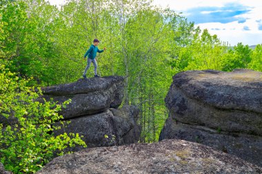 Genç yürüyüşçü kaya yapılarının tepesine atlıyor jeolojik alan, tarih öncesi okyanus çukuru şimdi yeşil orman ortamında. Rim rock, Batı Kanada Sedimentary Havzası, Alberta