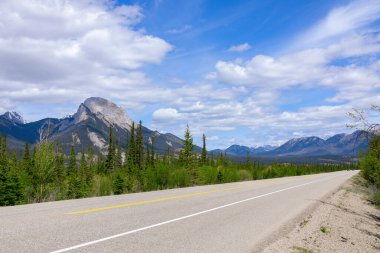 Empty highway among mountains and forests under the blue cloudy sky. Sunny summer day.