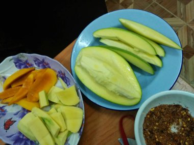 Slices of mango on the wooden table with chili sauce