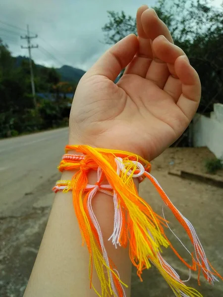 Hand with orange and yellow bracelets on a background of the road. The ceremony to tie holy thread on wrist.