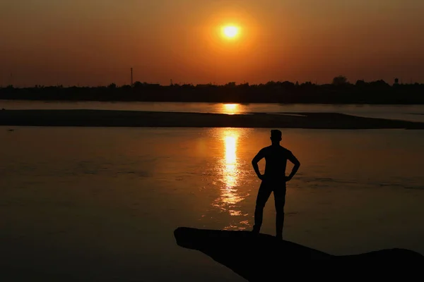 日落时一个人站在河岸上的轮廓 — 图库照片