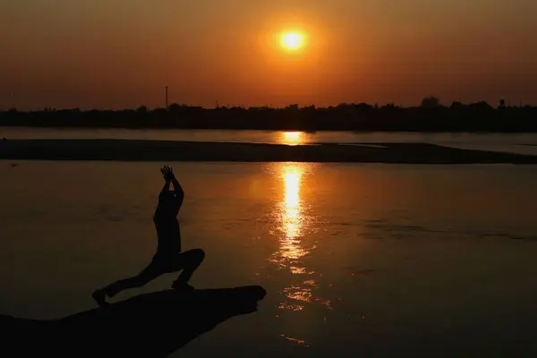 日落时 一个人在河边练瑜伽的轮廓 健康概念 — 图库照片