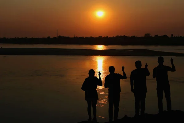 一群人的轮廓在夕阳西下的河岸上像一颗小小的心一样手拉手 友谊概念 — 图库照片