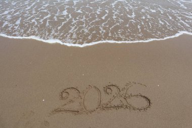 Yeni yıl 2026, deniz dalgası arka planında kumsalda yazılmış..