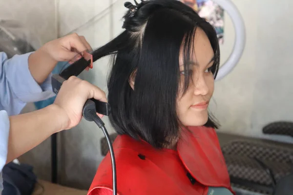 Hairdresser making hairstyle for young Asian woman.