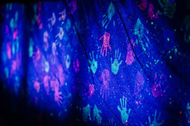 Yaratıcı sanat projeniz için siyah zemin üzerinde halojen ışığı olan çeşitli insan el izleri. Benzer el izlerinden oluşan soyut duvar kağıdı yumuşak ışıkla zıt tonlarda.