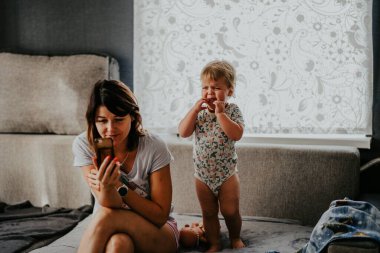 Annesi akıllı telefonuyla internette sörf yaptığı için annesi dikkat etmediği için kız ayakta ağlıyor. Gadget sorunları. Ebeveynlik sorunları.