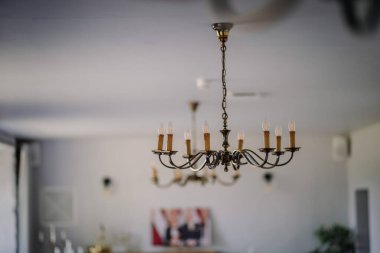 Mum ışığı şeklinde ampulleri olan antika bir avize tavanda asılı, gökyüzü manzaralı. Sahte süslemelerle metal açılış çerçevesi.