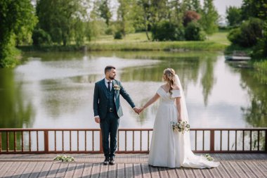 Göle karşı rıhtımda dikilirken yeni evlilerin birbirine bakışının yan görüntüsü.