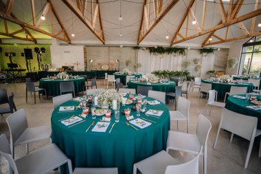 Düğün yeri yuvarlak masalar ve yeşil masa örtüleriyle süslenmiş. Eşsiz ve güzel görünüyor.