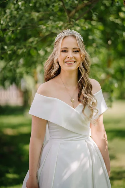 Beautiful bride stands on forest background. Rustic style. beautiful bride in delicate dress outdoors. Close up portrait of young bride in park in sunny weather wooded area
