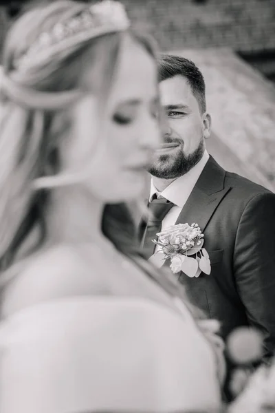 Selective focus of young attractive man wearing black suite and blurry woman in foreground wearing wedding gown. Concept for bride and groom wedding photography