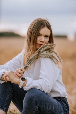 Kot pantolonlu ve beyaz gömlekli bir kadın çavdar tarlasında oturmuş elinde çavdar ekmeği kulakları tutuyordu. Tarım alanında..