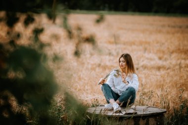 Kot pantolonlu ve beyaz gömlekli bir kadın tarımın kenarında bir kuyunun üzerinde oturuyor..