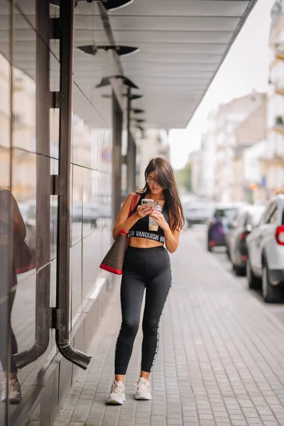 운동복을 여자가 가방을 거리에 자신의 전화기를 봅니다 — 스톡 사진
