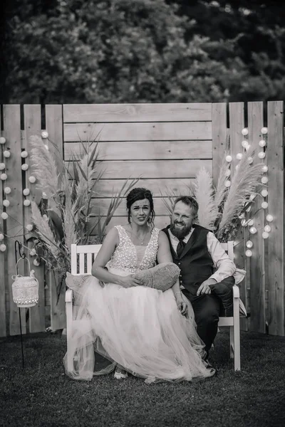 In this black and white picture, the bride and groom are seated on a bench in the photo corner, capturing a timeless and romantic moment of their special day.