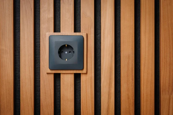 Black outlet plug on the wooden wall. Socket and European Power in the New Flat. Acoustic fluted wood panel.