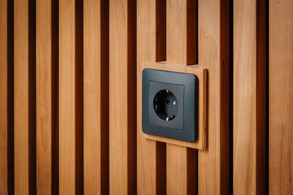 Black outlet plug on the wooden wall. Socket and European Power in the New Flat. Acoustic fluted wood panel.