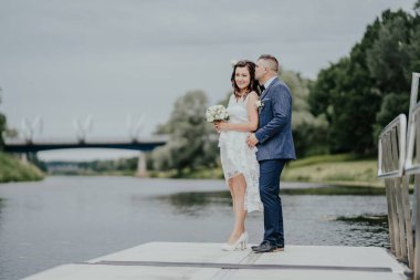 Evlendikleri gün nehir kenarında birbirlerine sarılıp eğlenen harika bir çift. Gelin ve damat birlikte mutlular.