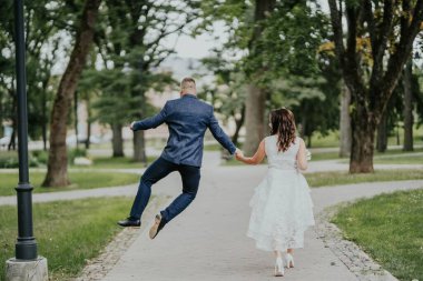 Gelin ve damat ağaçlı yolda yürüyor. Mutlu atlayışlar.