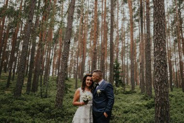 Gelin ve damat ormanda çam ağaçlarında. Damat gelinin alnından öper..