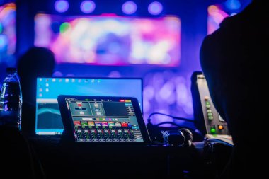 Ses kontrol konsoluna yakın çekim. Tablet ekranında ses düzeyleri çalışıyor. Ses mühendisi tableti eline alır. Sahnedeki ses parametrelerinin uzaktan denetimi