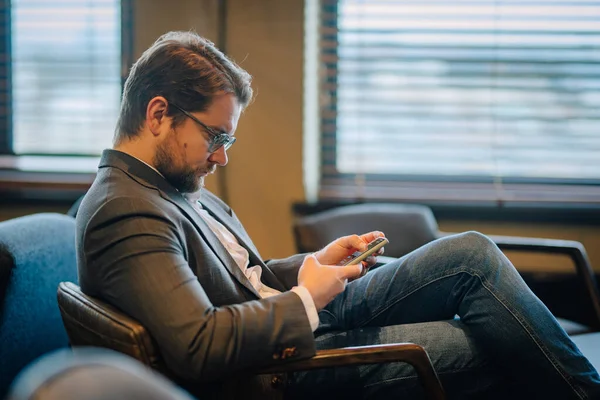 Young businessman sitting at hotel bar reading smartphone texts