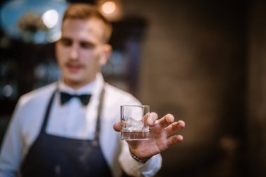 İçki için şeffaf boş bardakları tutan bir erkek barmenin elleri. Bulanık çubuk arkaplanı