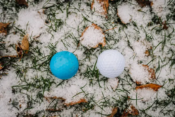 Two golf balls stand in the snow to see the difference as you can see. White and blue. Golf game in the snow.