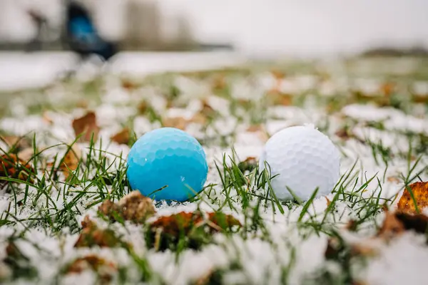 Two golf balls stand in the snow to see the difference as you can see. White and blue. Golf game in the snow.