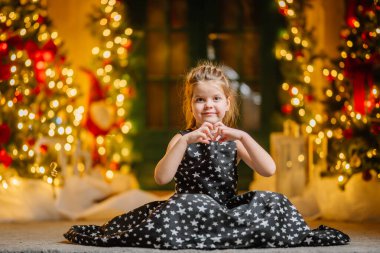 Siyah elbiseli, Noel atmosferinde yıldızlar olan küçük bir kız. Kız Noel için mutlu. Noel süslemeleri.