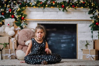 Siyah elbiseli, Noel atmosferinde yıldızlar olan küçük bir kız. Kız Noel için mutlu. Noel süsleri. Resim çekmekten hoşlanmadığı için alınıyor.