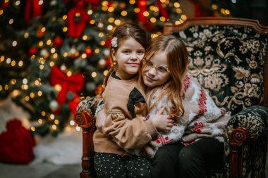 Kız kardeşler Noel süslemelerinde zarif bir sandalyede oturuyorlar