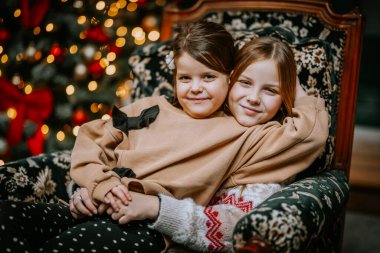 Kız kardeşler Noel süslemelerinde zarif bir sandalyede oturuyorlar