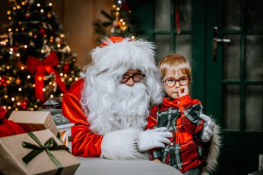 Kucağında tatlı bir çocukla Noel Baba bir sandalyede otururken Noel dileklerini dinler..