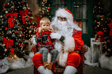 Kucağında tatlı bir çocukla Noel Baba bir sandalyede otururken Noel dileklerini dinler..