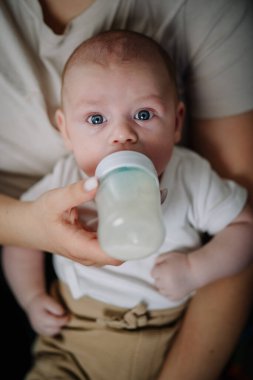 Bebek besleyici yemeğin tadını çıkarıyor. Anne bebeği besliyor. Dadı mama emzirmeye alternatif olarak küçük çocuğu besler. Bebek ya da kız kanepede yatar ve plastik şişeden süt içer.