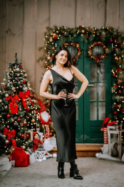 Noel odasının arka planında siyah bir elbiseyle poz veren, akşam makyajı ve saç stili olan varlıklı bir kadının portresi. Lüks bir yaşam tarzı. Noel tatili kavramı