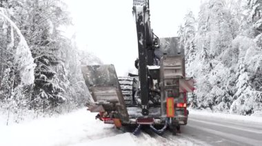 Valmiera, Letonya - 8 Aralık 2023 - Ağır makineler kış aylarında orman makinelerini taşır. Yol kenarındaki tehlikeli ağaçların kaldırılması.