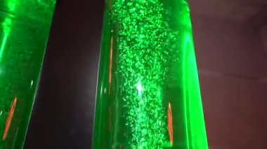 LED 'ler tarafından aydınlatılan ikiz yeşil kabarcıklı sıvı borular, geniş bir kapalı alanda koyu bir zemin üzerine kurulmuş, muhtemelen bir bilim sergisi..