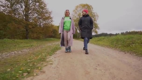 2人の女性が 田舎や公園の設定のように見える汚れた道を歩いています 彼らは涼しい天気の服装を着て それが秋や春かもしれないことを示唆しています — ストック動画