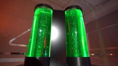 LED 'ler tarafından aydınlatılan ikiz yeşil kabarcıklı sıvı borular, geniş bir kapalı alanda koyu bir zemin üzerine kurulmuş, muhtemelen bir bilim sergisi..