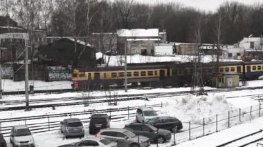  Sarı ve mavi yolcu treninin karla kaplı bir tren istasyonundan geçtiği gündüz sahnesi..