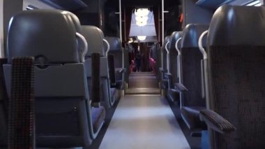  Merkezi bir koridorun her iki tarafında sıralı koltukları olan modern bir trenin içi. Koltuklar konfor için tasarlandı, başlıklar ve döşemeler desenli.