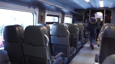  Merkezi bir koridorun her iki tarafında sıralı koltukları olan modern bir trenin içi. Koltuklar konfor için tasarlandı, başlıklar ve döşemeler desenli.