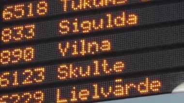 Elektronik tren kalkış panosunun yakın çekim görüntüsü tren numaralarını, varış noktalarını ve kalkış zamanlarını gösteriyor. Bilgi turuncu LED ışıklarda siyah bir arkaplan ile gösterilir. 