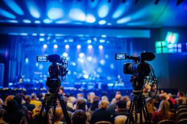 Valmiera, Letonya - 28 Aralık 2023 - Tripodlar üzerinde iki profesyonel video kamera ön planda seyirci ve arka tarafta sahne ışıkları ile bir konser kaydediyor.