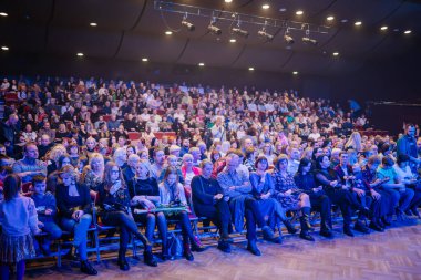 Valmiera, Letonya - 28 Aralık 2023 - Bir tiyatroda tam seyirci kitlesi, çeşitli yaşlardan insanlar sahneye bakıyor, sahne ışıklarıyla aydınlatılıyor.