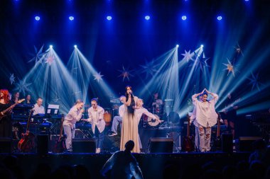 Valmiera, Letonya - 28 Aralık 2023 - Sahnede bir grubun sahne aldığı canlı bir konser sahnesi, dramatik mavi ışıklar ve yıldız süslemeleriyle aydınlatılıyor..