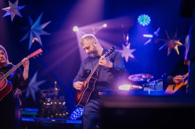 Valmiera, Letonya - 28 Aralık 2023 - Gitar çalan müzisyenler sahne arkasında parlak mavi sahne ışıkları ve yıldız süslemeleri ile.